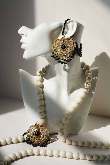 Ira - Chandbali Set with matching maang tikka in gold-tone finish, black beads, and CZ stones displayed on a white mannequin bust.