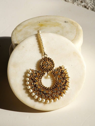 Laila Maang Tikka in antique gold with circular motifs and pearl accents, styled on a white marble background.