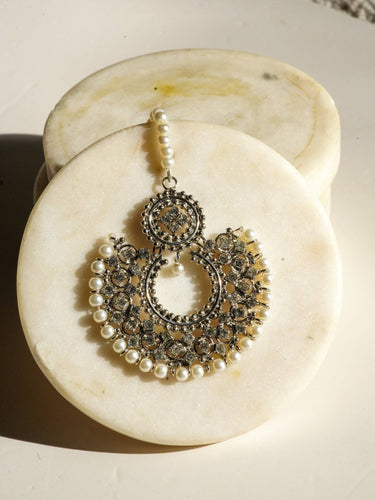 Laila Maang Tikka in antique gold with circular design, white stones, and pearl detailing, styled on a marble background.