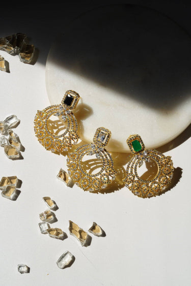 The Mia - Dainty Chandbali Earrings trio in black, white, and green CZ stones, displayed on a round marble slab with scattered crystals.