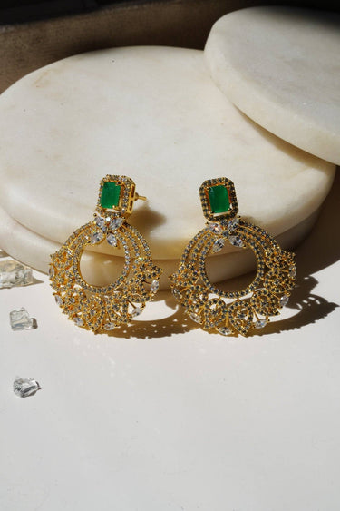Pair of The Mia - Dainty Chandbali Earrings with green CZ stones, placed on a white marble slab under soft natural light.