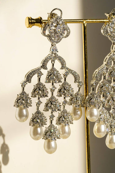 Single Sahara Chandelier Earring on gold stand, showcasing rhodium-plated craftsmanship and shimmering pearl accents in natural light.