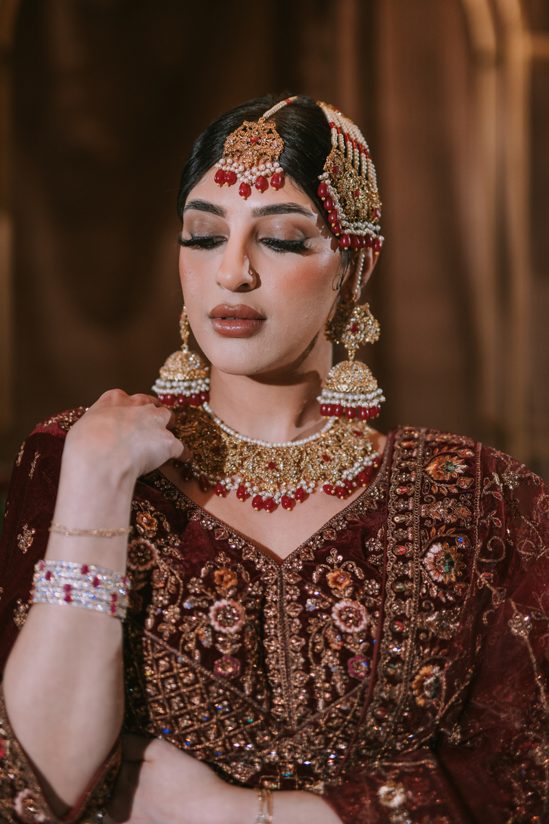 Gold-plated bridal jewelry set with red stone accents including choker necklace, jhumka earrings, tikka, and passa - South Asian bridal jewelry - Inaury