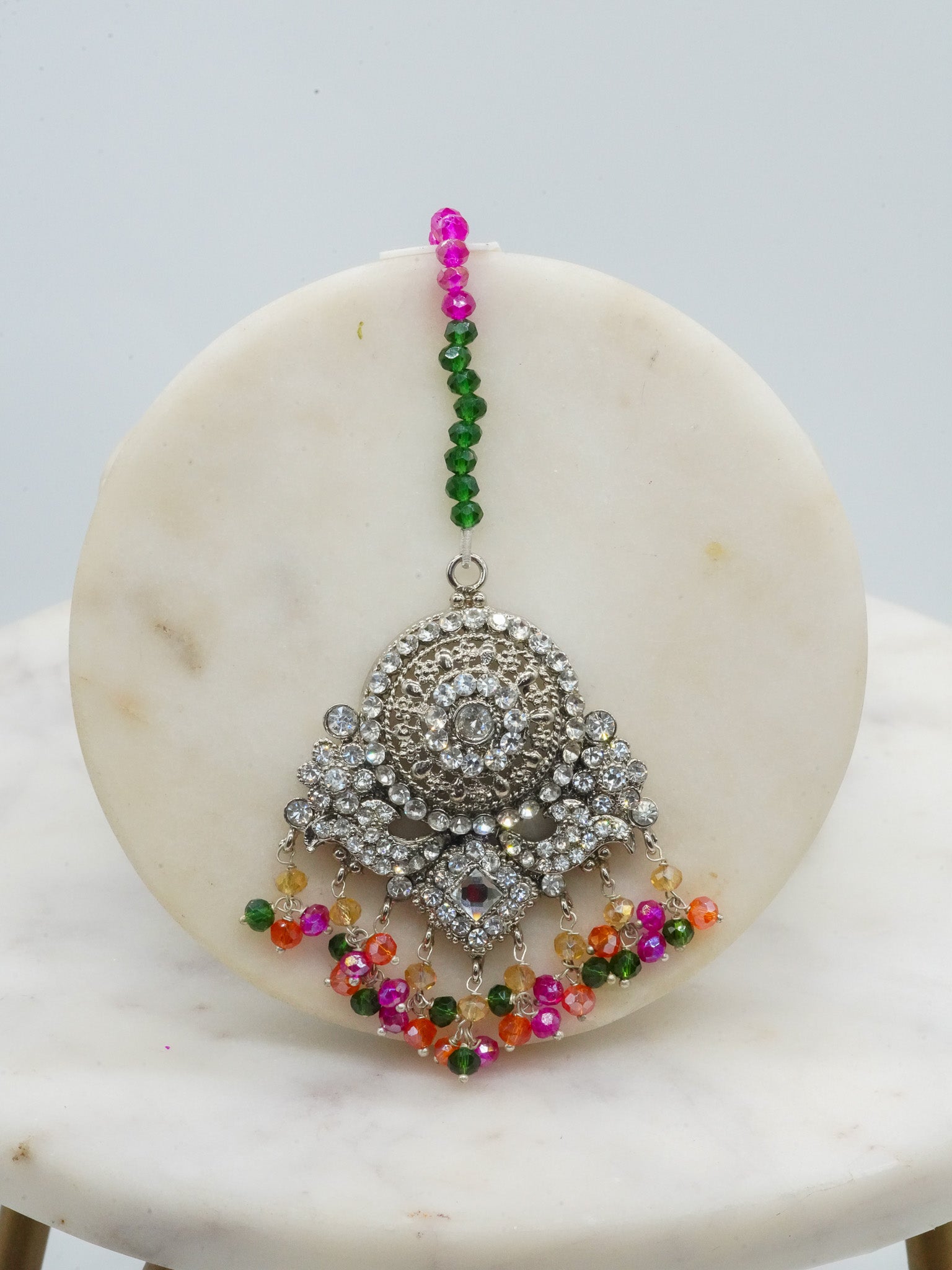 Maang tikka from Namar Choker Necklace Set with multicolor beads and silver CZ stones, displayed on marble disc.