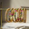 Anayasa 7-piece Gold Plated Bangle Set with colorful diamante accents, displayed on a gold stand for elegant jewelry presentation.