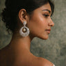 Woman wearing large, ornate earrings with a neutral background