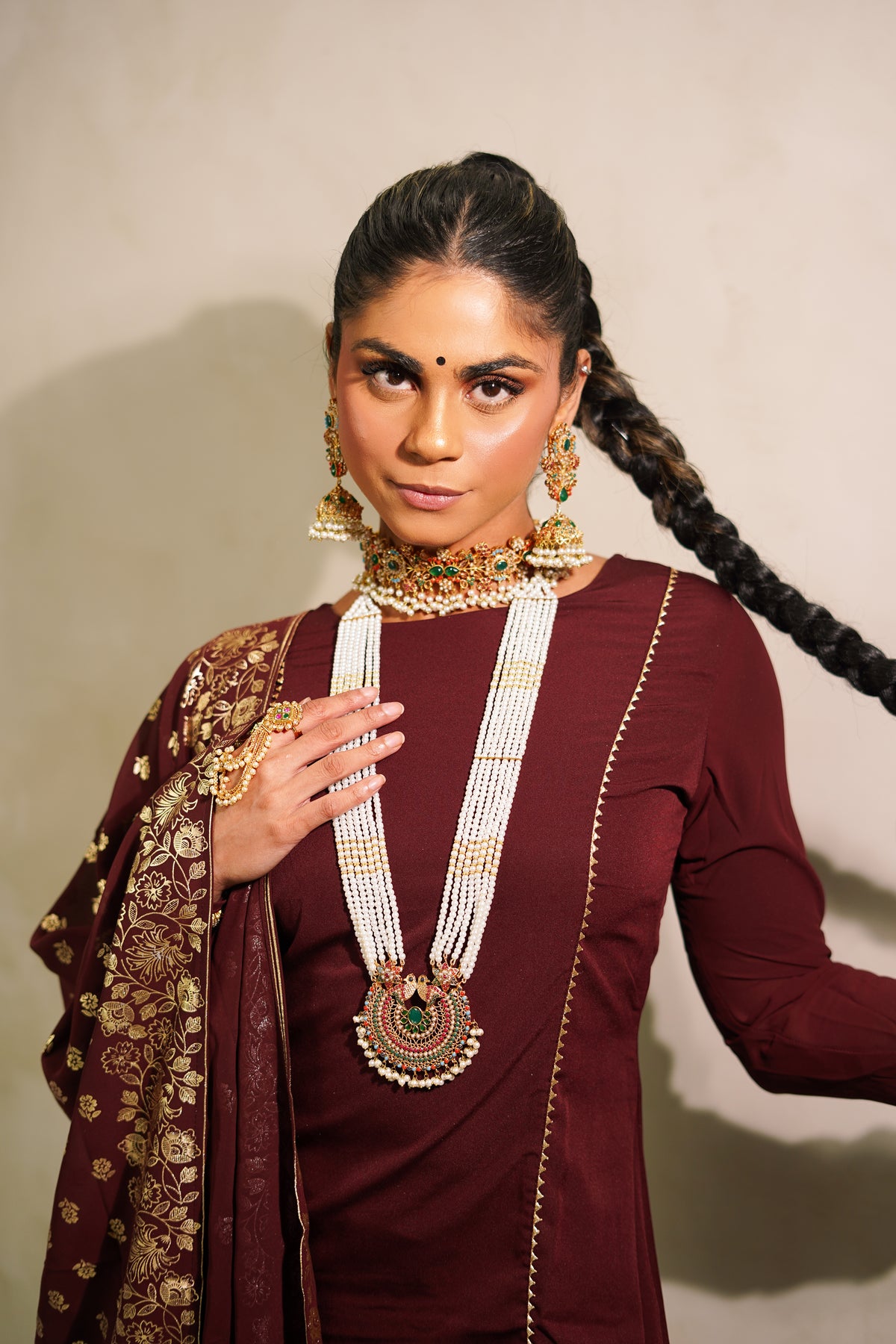 Woman in traditional attire with jewelry against a plain background