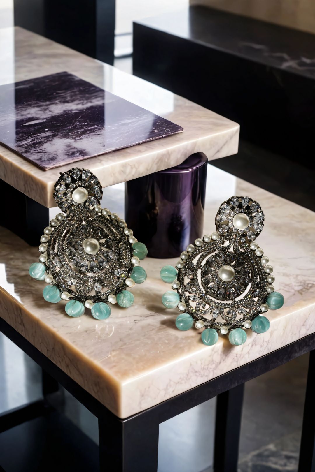 Navya Black Plated Chandbali Earrings with green beads and ornate design, displayed on marble table for luxury jewelry appeal.