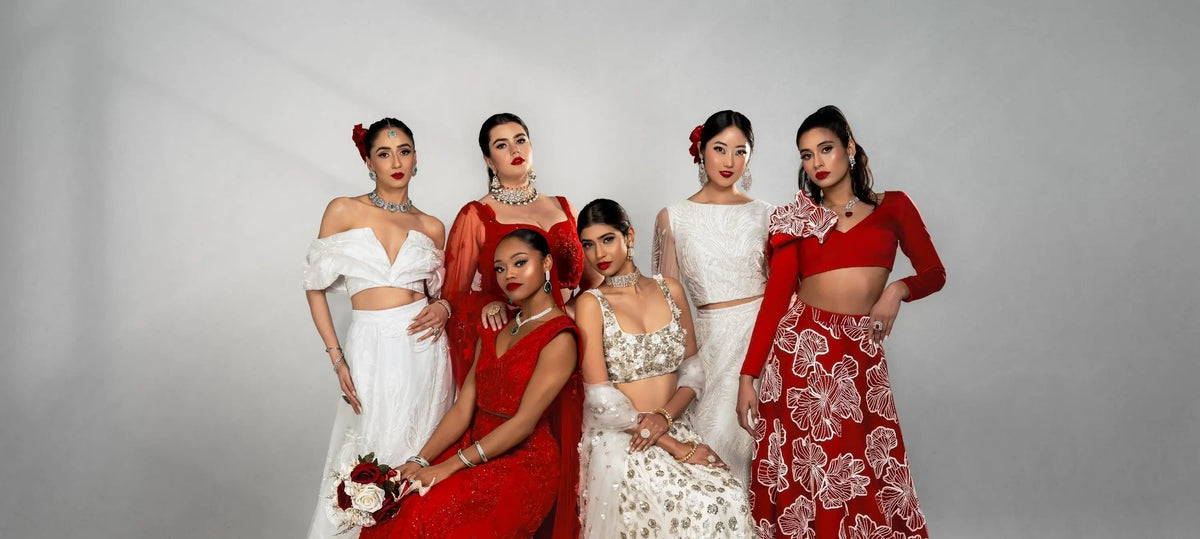 Group of women in traditional red and white with outfits and Indian jewelry from Inaury.com posing against a gray background.