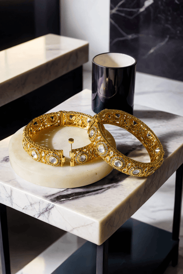 Tamina Moissanite Polki Bangles - Heritage Style | Openable gold bangles placed on round marble slab, reflecting regal craftsmanship.