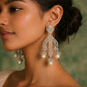Woman wearing elegant silver earrings with pearls against a green background