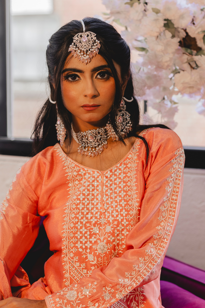 Model wearing Noreen Choker Necklace Set - Elegant Pakistani Bridal Jewels in silver with pink stones, styled with traditional peach attire.