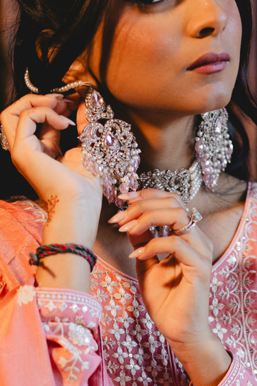 Model adjusting earring from Noreen Choker Necklace Set - Elegant Pakistani Bridal Jewels, highlighting craftsmanship and pink gemstone details.