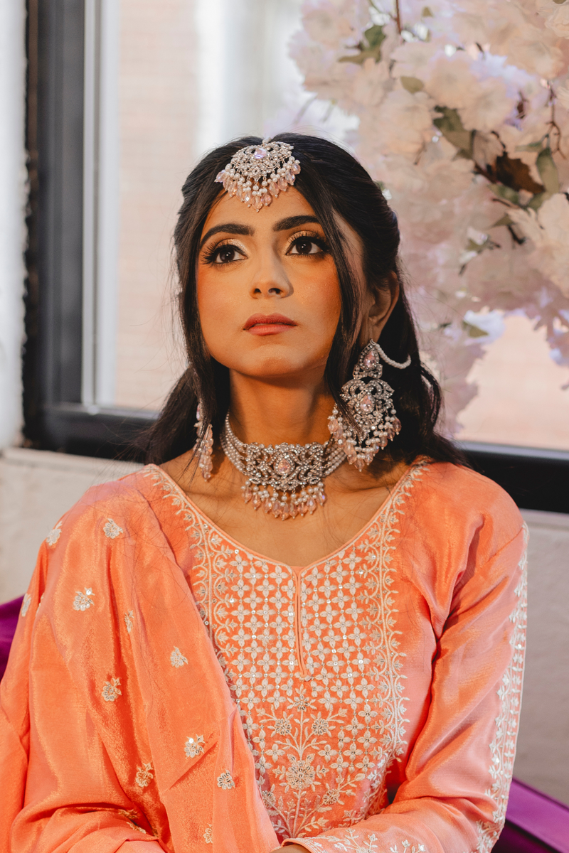 Model in peach outfit wearing Noreen Choker Necklace Set - Elegant Pakistani Bridal Jewels with silver and pink embellishments for bridal styling.