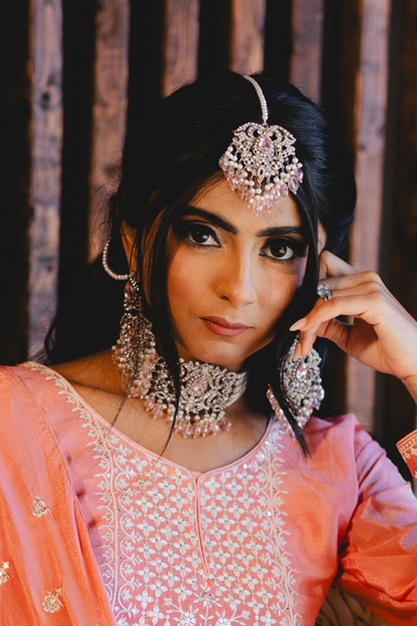 Model posing in Noreen Choker Necklace Set - Elegant Pakistani Bridal Jewels with pink stones, styled with traditional peach embroidered dress.