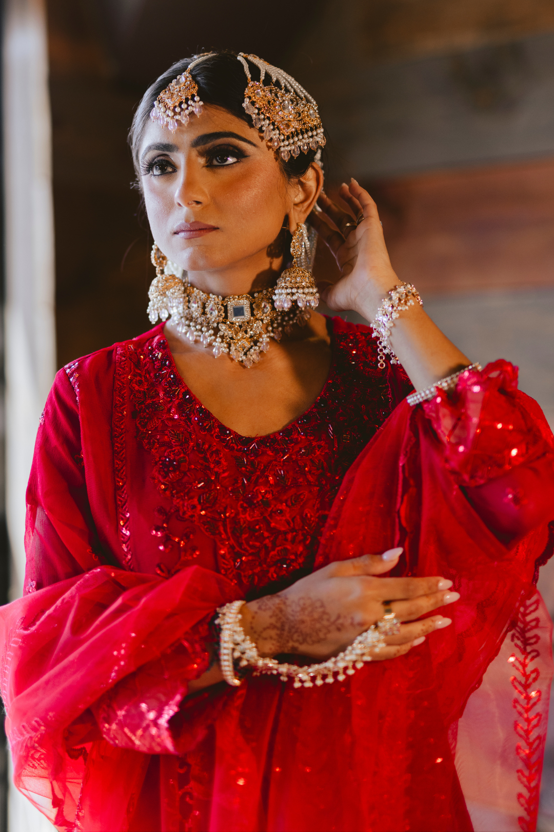 Desi bride wearing Sareena Mirror Choker Set - Zircon & Pearl in silver with mirror work, styled with red bridal attire for formal occasions.