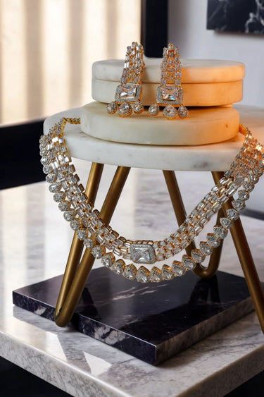 Zaina Double Layered AD Necklace Set with gold plating and earrings styled on a marble table. A luxurious jewelry set under $200.