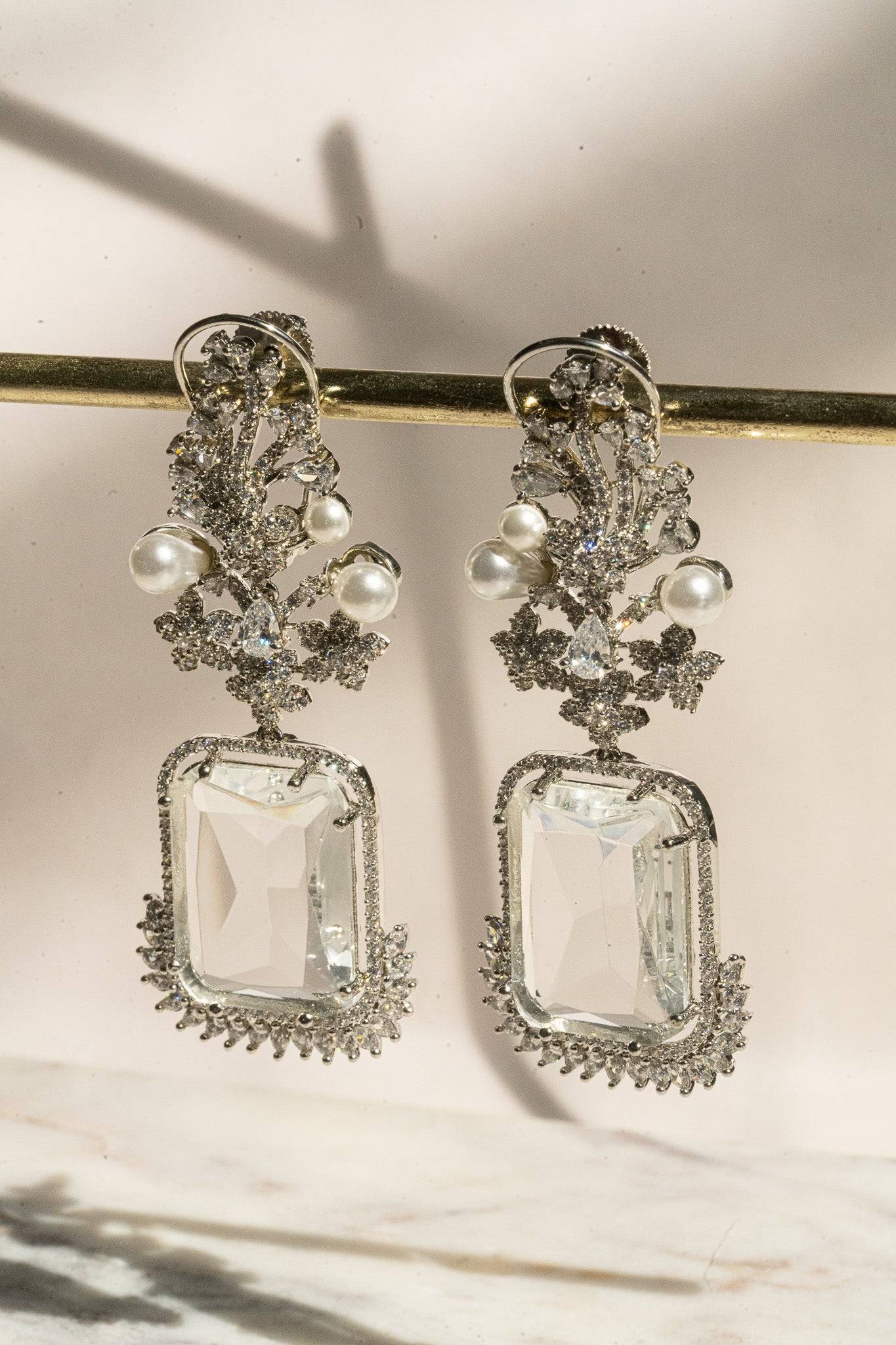 Side view of Aayat Statement Earrings in crystal white showcasing intricate floral design and sparkling pavé halo. Rhodium-plated dangle earrings.