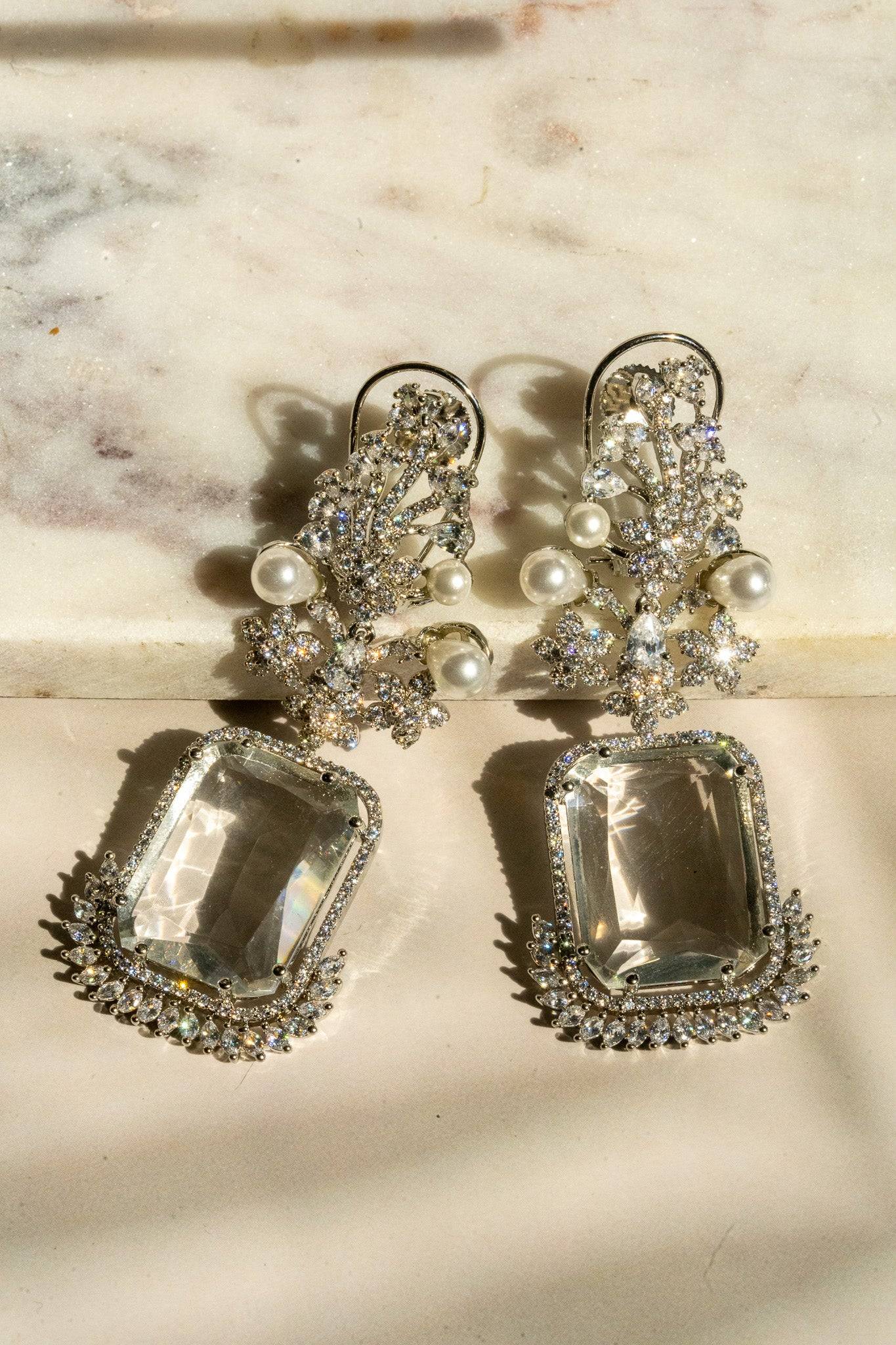 Flat lay of Aayat Statement Earrings in crystal white with pavé halo, floral motifs, and pearl accents. South Asian-inspired jewelry.