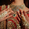 Close-up of a person wearing intricate jIndian bridal ewelry including a necklace, earrings, and bangles.