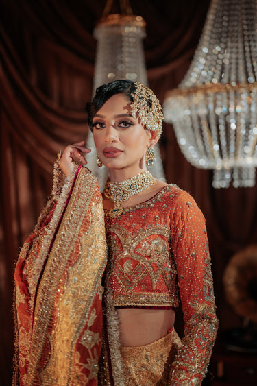 A woman wearing an orange lehenga styled with the Afsoon bridal set featuring moissanite polki stones with choker, earrings, and jhoomer from Inaury.com