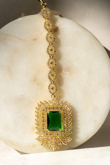 Alora Maang Tikka in gold plating with green crystal-cut centerpiece and AD detailing, perfect for traditional styling.