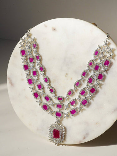 Amisha Triple Layer Diamante Accent AD Necklace Set in gold or rhodium-plated silver finish with color options of silver & sapphire blue, silver & green, gold & green, and silver & ruby, featuring floral and cushion cut stone patterns with matching earrings.