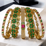 Arika 7-piece floral gold-plated bangle set with emerald and ruby stones displayed in a fan layout. Ideal for weddings and celebrations.