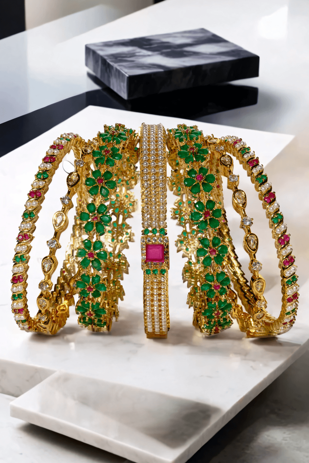 Arika 7-piece floral gold-plated bangle set with emerald and ruby stones displayed in a fan layout. Ideal for weddings and celebrations.