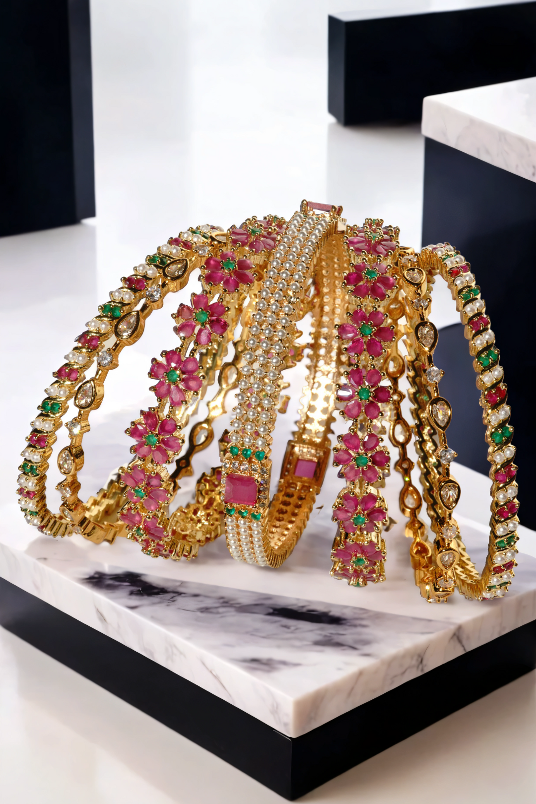 Full view of Arika 7-piece gold-plated bangle set with floral ruby and emerald accents. Perfect for bridal and traditional fashion.