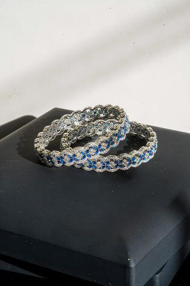 Rhodium plated Indian bangles with sapphire blue and white stones on a black jewelry box.