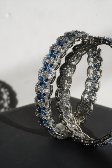 Pair of silver hoop earrings with blue gemstones on a dark surface.