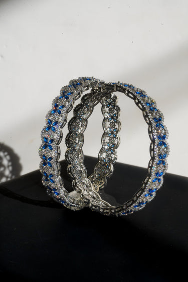 Pair of rhodium plated silver bangles with sapphire blue gemstones on a black surface