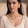 Model wearing gold plated Kundan double layer necklace set with matching stud earrings and an ivory embroidered outfit