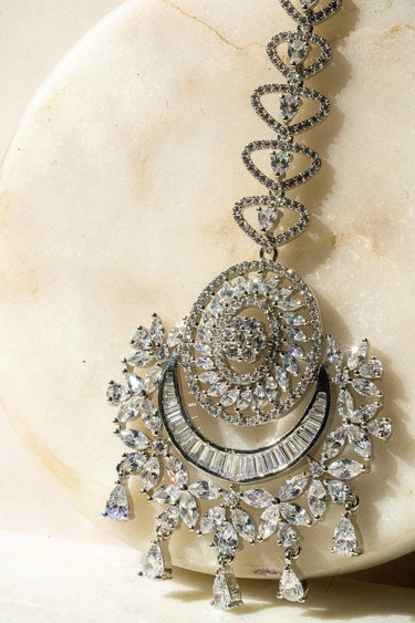 Iliyana Maang Tikka in rhodium finish with CZ stones, featuring a floral crescent design. Ideal for bridal and festive hair styling by Inaury.