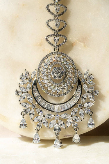 Iliyana Maang Tikka in rhodium finish with CZ stones, featuring a floral crescent design. Ideal for bridal and festive hair styling by Inaury.