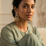 A front facing studio portrait of a model styling the gold plated Aadhya Kundan glass polki earrings with a sage green embroidered outfit.