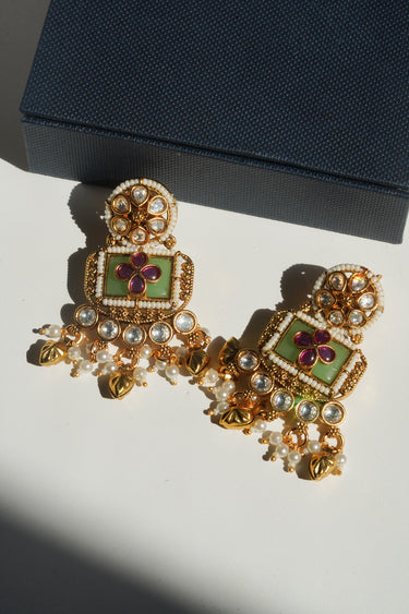 A studio presentation view of the Aadhya green and ruby kundan drop earrings showcased next to a luxury dark blue textured jewelry box.