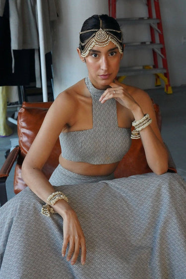 Close-up of the Aliya Jhumka Bangle Bracelet in antique gold with faux pearl beadwork, worn on a seated model in a grey contemporary South Asian outfit.