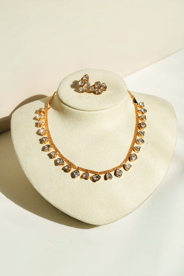 The complete Dilara gold-plated necklace featuring a strand of heart-cut Moissanite stones in a Kundan setting displayed on a cream velvet neck bust with its matching cluster stud earrings.