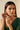 Close-up front portrait of a model adjusting the Kavya gold-plated crescent statement earrings featuring ruby centerpieces and green glass drops.