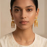 A clean front portrait of a model styling the gold plated Lara handcrafted filigree jhumka earrings paired with an elegant cream embroidered dress.