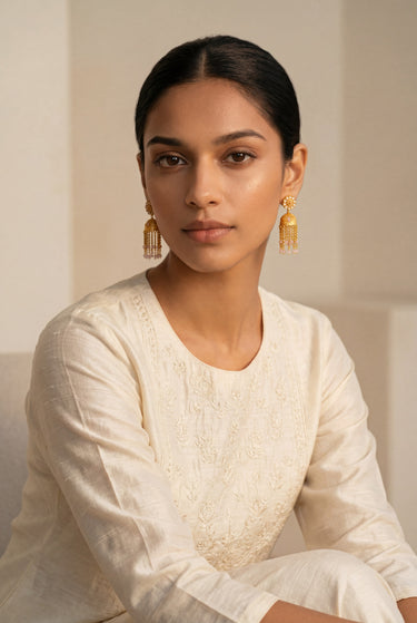 A three quarter lifestyle portrait of a model wearing the Lara handcrafted gold jhumka earrings to display their length and fluid chain movement.