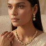 An elegant three-quarter lifestyle portrait of a model showcasing the gold-plated Mehr single-strand teardrop Moissanite necklace and matching cascading triple-tier drop earrings.