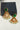 A studio flat lay presentation of the gold-plated Mira peacock earrings in the emerald green colorway featuring matching green top stones and glass bead drops.