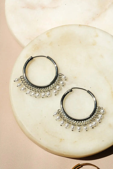 A close up studio shot showing the pair of rhodium plated Sia hoops adorned with delicate white seed pearls on white marble.