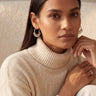 A front view studio portrait of a model styling the silver rhodium Sia beaded hoop earrings.