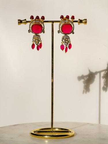 A detailed display pair view of the Sweta matching 1.5-inch gold-plated top dangler earrings highlighting the emerald-cut red center stones.