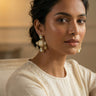 A close up three quarter lifestyle portrait of a model styling the mehndi gold plated Zoe geometric drop earrings with a cream colored outfit.
