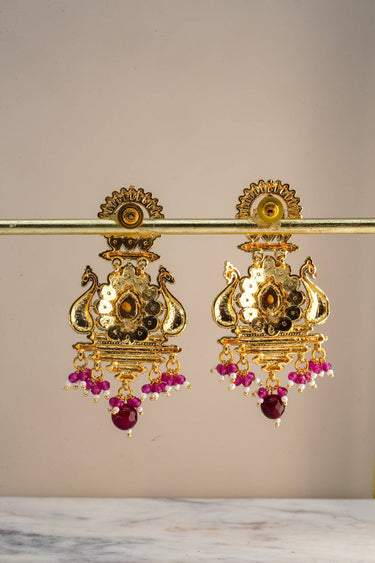 Back view of Inaury Adrita Kundan Meenakari Peacock Drop Earrings on gold bar stand — reverse of peacock body and push-back stud closure with ruby bead drops visible